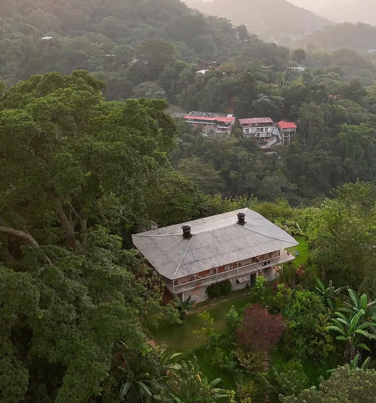 Looking down on a hostel roof in a jungle valley, with more red-roofed buildings on the hillside above