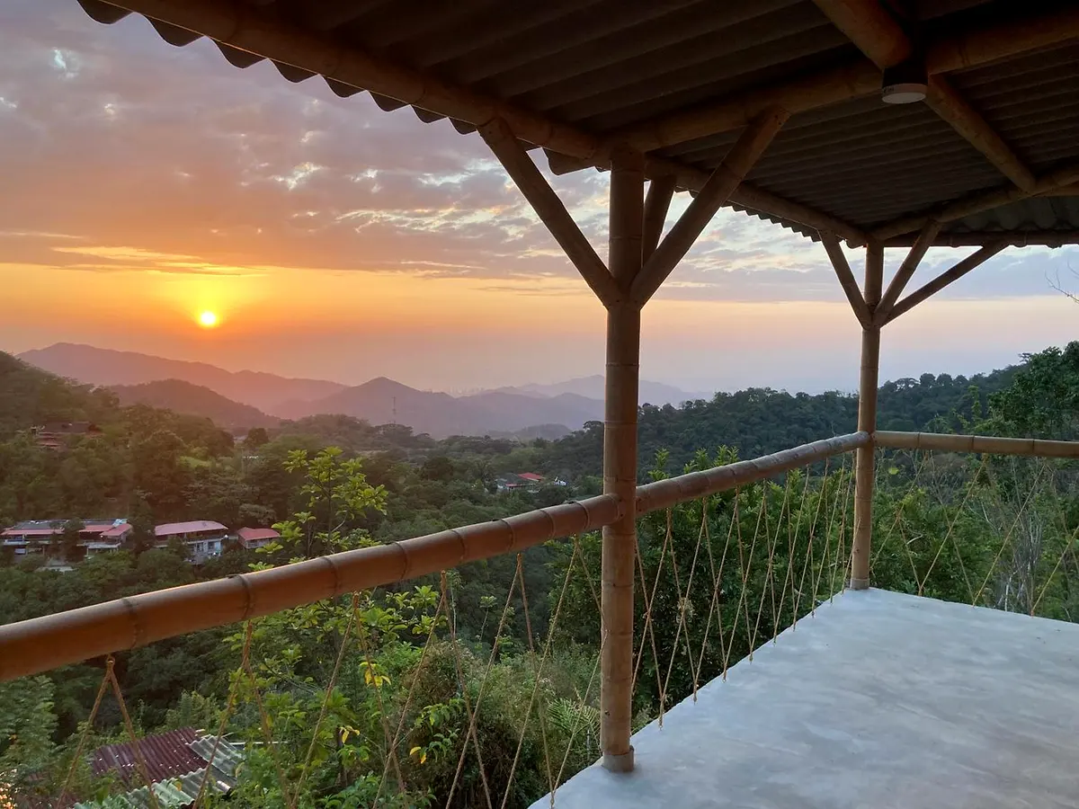Sunset seen from a bamboo balcony, the sun low over hazy mountains with hostel roofs among the trees below
