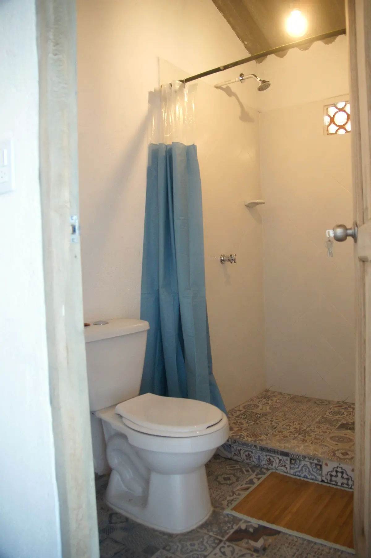 A simple bathroom with a white toilet, a blue shower curtain and a pebble-tiled shower floor