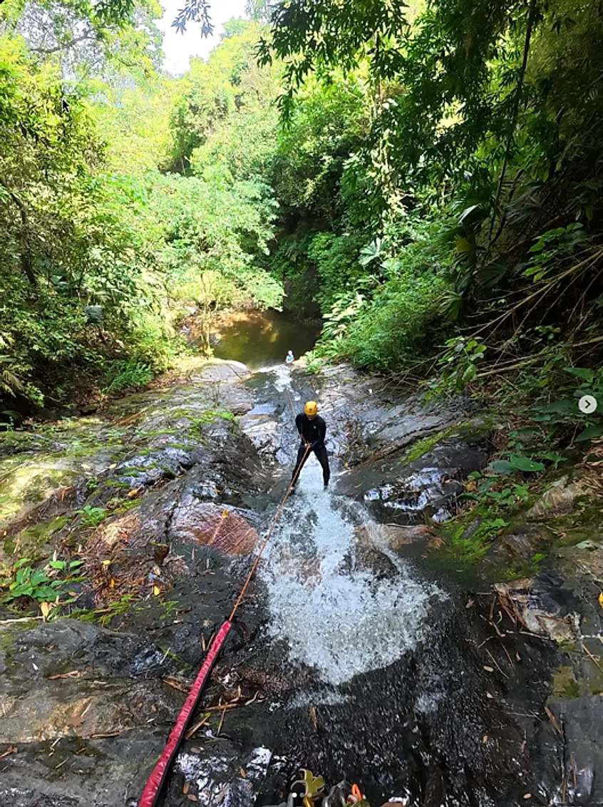 Looking down a jungle gorge as a canyoner descends a waterfall on a red rope