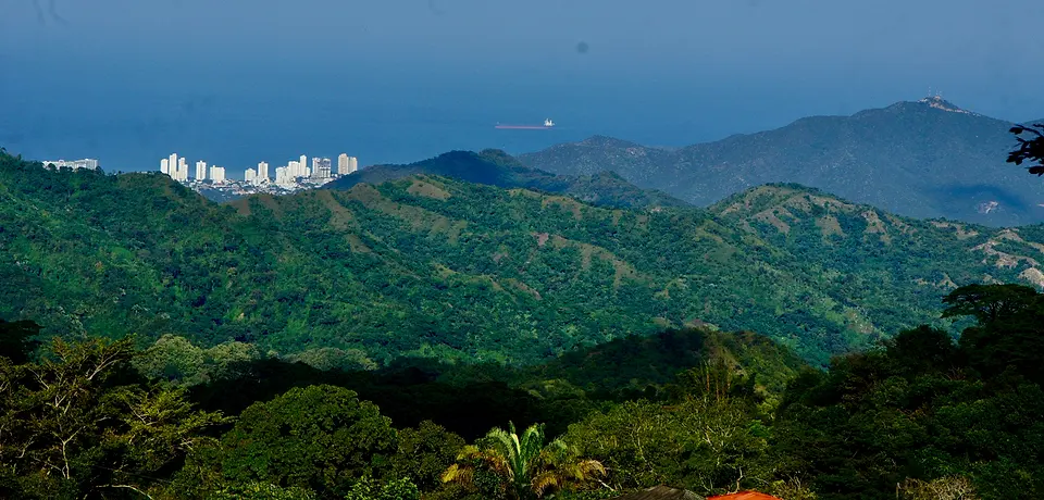 Panorama from the hostel over green jungle ridges to the white towers of Santa Marta, the bay and a ship on the Caribbean