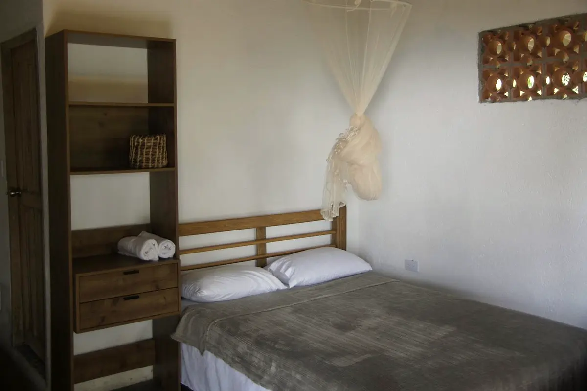 Deluxe double room: double bed under a white mosquito net with wooden shelves and folded towels beside it
