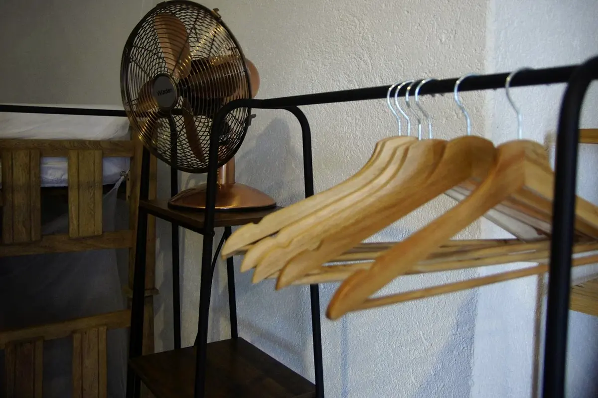 A copper desk fan and wooden hangers on a black rail beside a wooden bunk