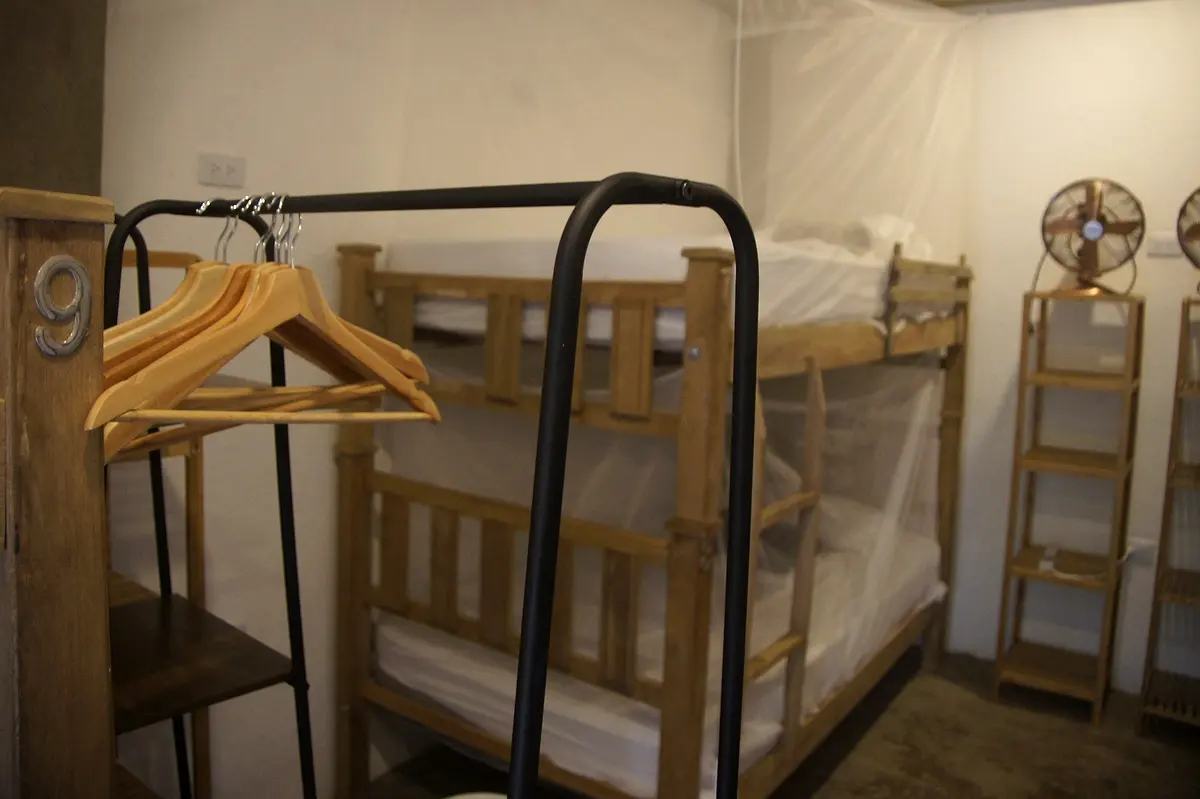 Mixed dormitory: a numbered bunk post, wooden hangers on a black rail and a bunk bed with mosquito net behind