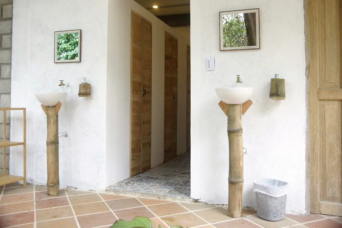 Shared washbasins on bamboo pedestals with mirrors along a tiled corridor with wooden doors