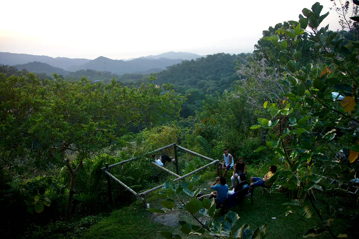 Guests relaxing at the edge of the garden beside a hammock frame, looking out over a deep jungle valley