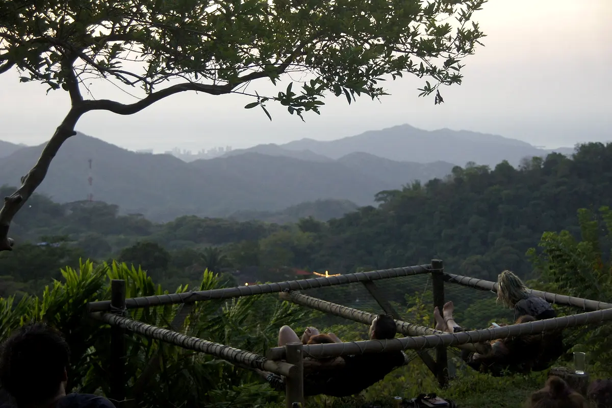 Hammocks and a wooden rail at dusk under a large tree, with the valley fading into blue haze