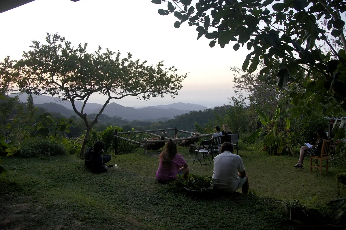 Guests sitting on the lawn under a spreading tree at dusk, the mountains turning blue behind them