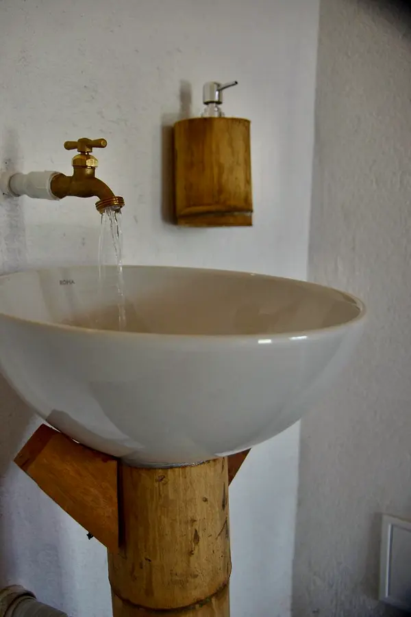 Close-up of a round white washbasin on a bamboo pedestal with a brass tap running
