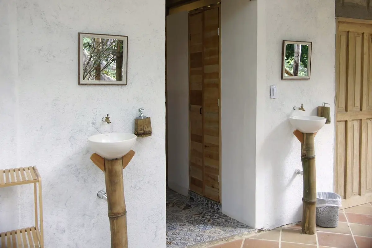 Shared washbasins on bamboo pedestals with small mirrors, beside wooden bathroom doors and a tiled floor