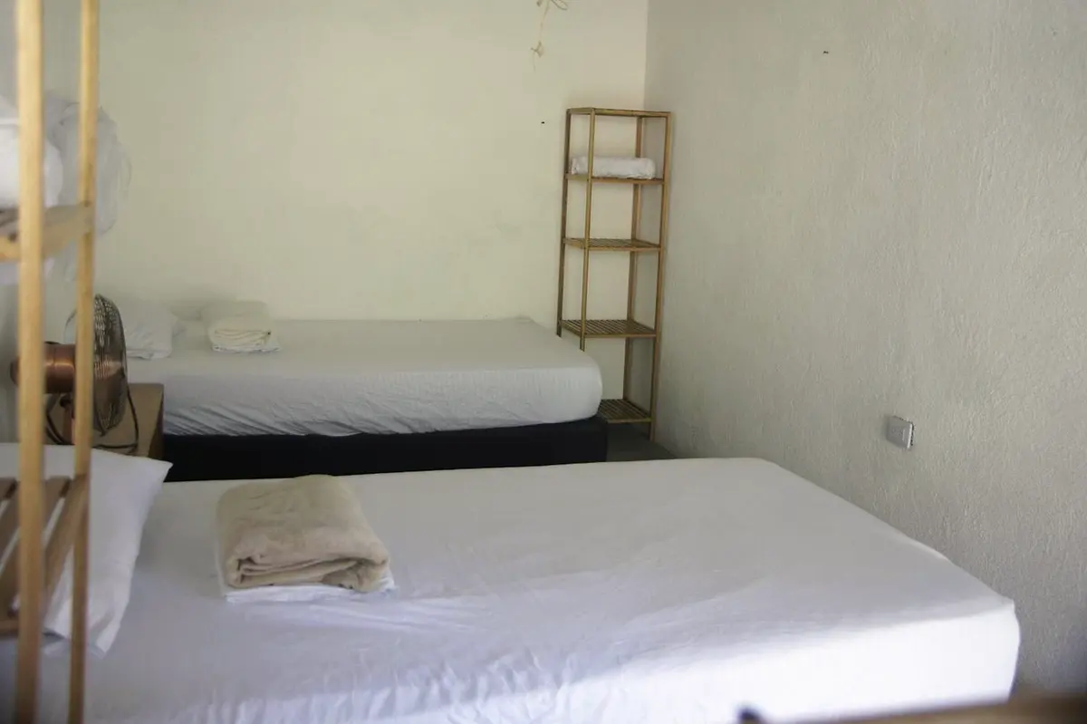 Standard twin room: two single beds with white sheets and folded towels against white walls, with a small wooden shelf