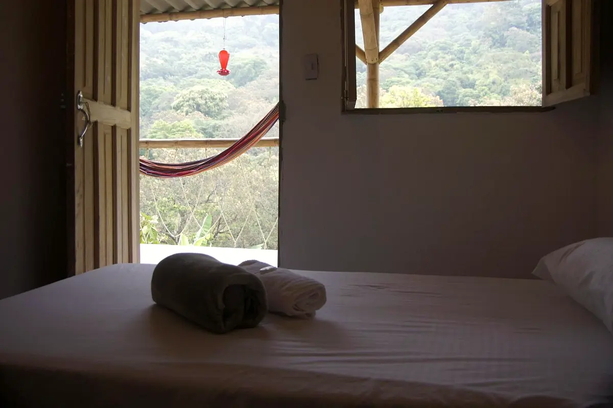 Standard twin room: a bed with rolled towels in front of an open door and window onto the veranda, a hammock and the jungle