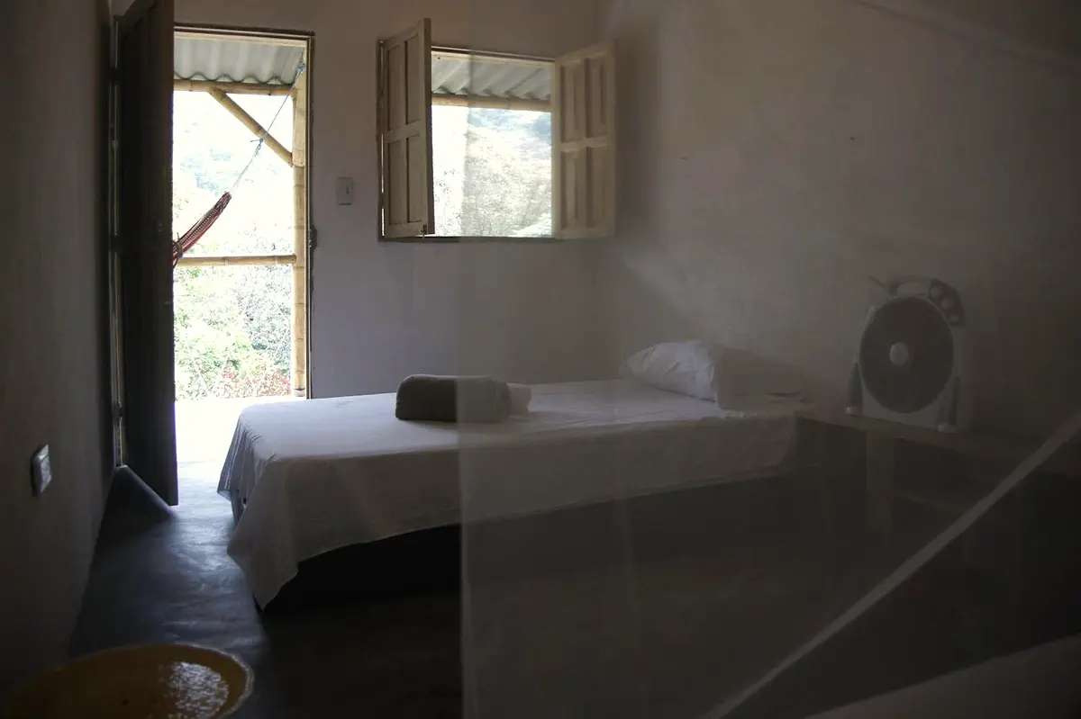 Standard twin room in soft light: a bed under a mosquito net, a fan, and the open veranda door and window
