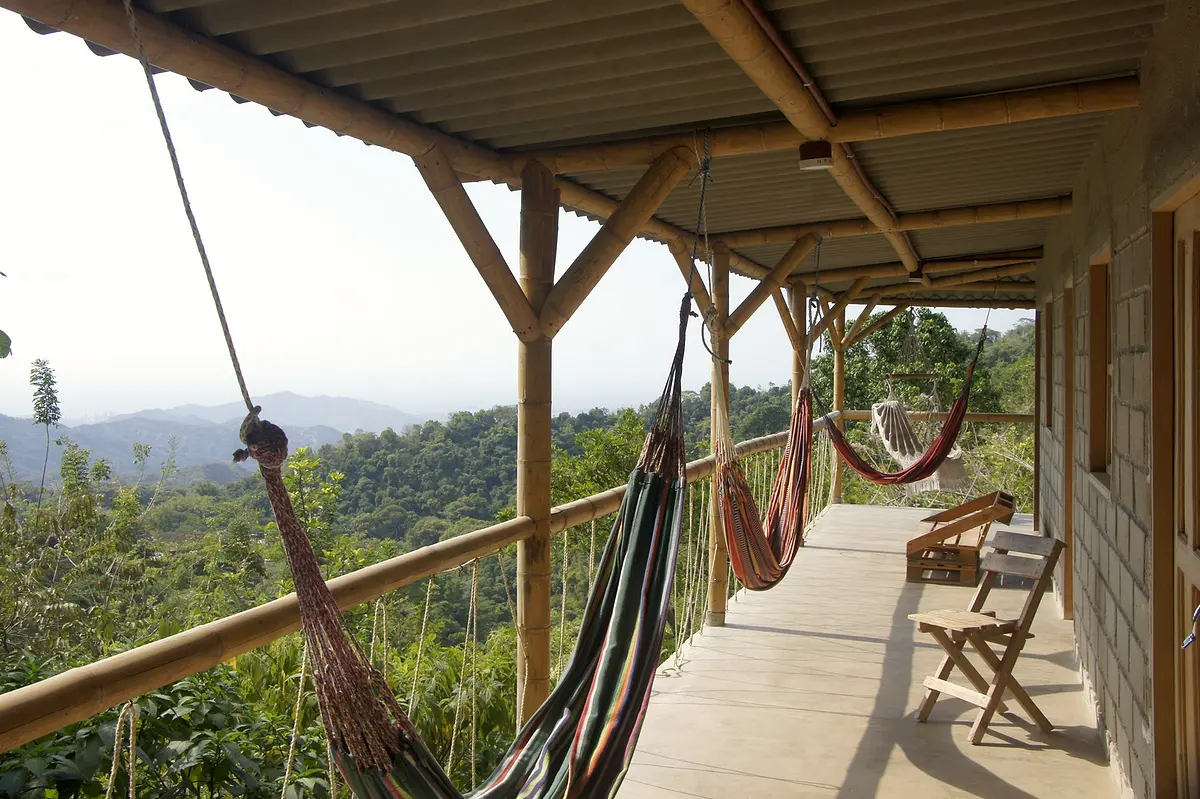 A long wooden veranda with hammocks strung between the posts and the jungle and sky beyond the railing
