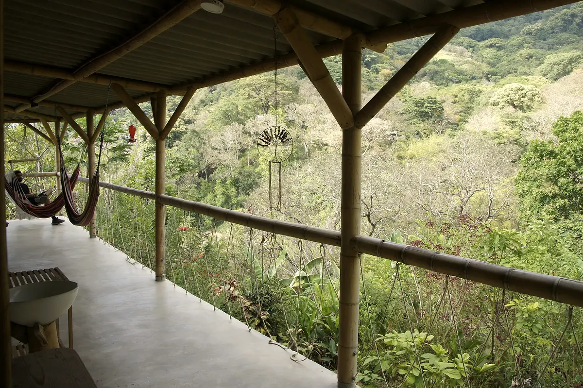 A covered veranda with a hammock at the far end, opening onto forested hills